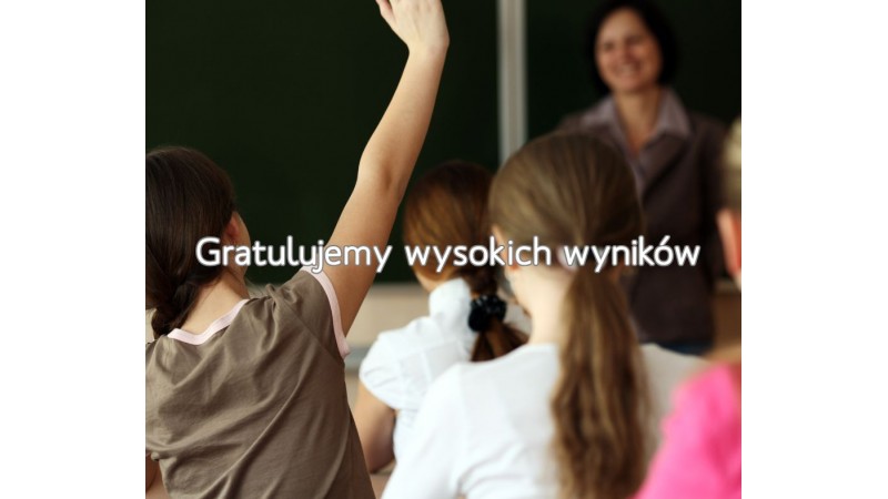 Uczniowie podczas lekcji w klasie szkolnej. Grafika zawiera napis: „Gratulujemy wysokich wyników”.